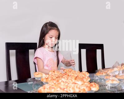 Adorable petite fille emballage séparé saucisse de porc cuite avec pain de mayonnaise, cuisine domestique, enfant aidant ses parents Banque D'Images