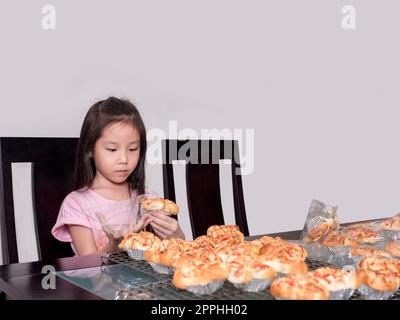 Adorable petite fille emballage séparé saucisse de porc cuite avec pain de mayonnaise, cuisine domestique, enfant aidant ses parents Banque D'Images