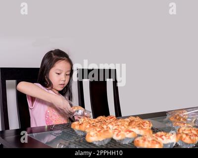 Adorable petite fille emballage séparé saucisse de porc cuite avec pain de mayonnaise, cuisine domestique, enfant aidant ses parents Banque D'Images