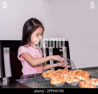 Adorable petite fille emballage séparé saucisse de porc cuite avec pain de mayonnaise, cuisine domestique, enfant aidant ses parents Banque D'Images