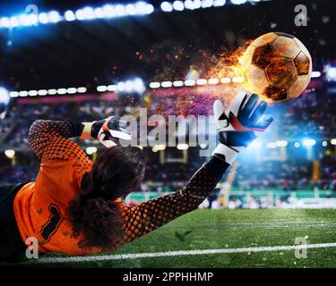 Le gardien de but attrape le ballon de feu dans le stade pendant un match de football. Banque D'Images