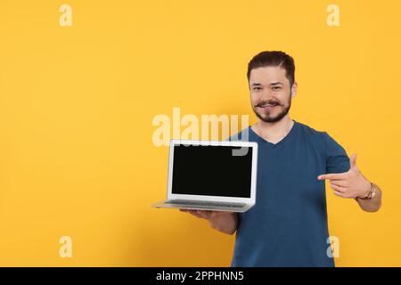 Homme émotionnel pointant vers un ordinateur portable sur fond orange. Espace pour le texte Banque D'Images