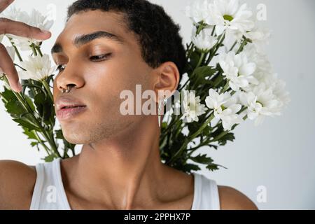 portrait de l'homme afro-américain avec le perçage de l'argent posant près de fleurs blanches fraîches isolées sur gris, image de stock Banque D'Images