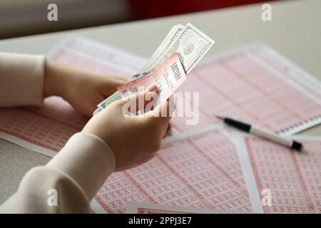 Une jeune femme tient le billet de loterie avec une rangée complète de chiffres et de billets de dollar sur le fond des feuilles vierges de loterie Banque D'Images