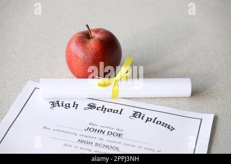 Un diplôme d'études secondaires repose sur la table avec un petit rouleau et une pomme rouge. Documents éducatifs Banque D'Images