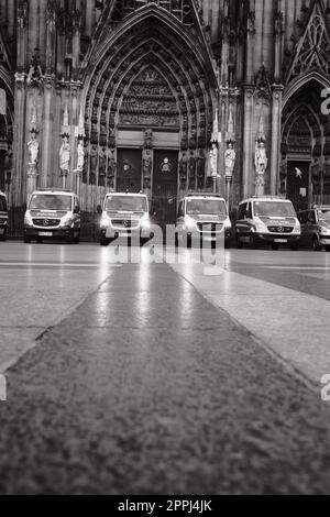 Photo en niveaux de gris d'une rangée de voitures de police Mercedes-Benz Sprinter en face de la cathédrale de Cologne en Allemagne Banque D'Images