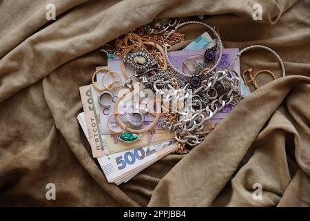 Bouquet de bijoux volés et de l'argent sur tissu d'uniforme militaire. Pillage par des soldats russes dans les villes ukrainiennes lors de l'attaque russe sur l'Ukraine. Maraudeurs et pilleurs Banque D'Images