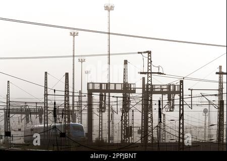 Un train de voyageurs en brume et en contre-jour sur une piste avec des fils et des poteaux aériens Banque D'Images