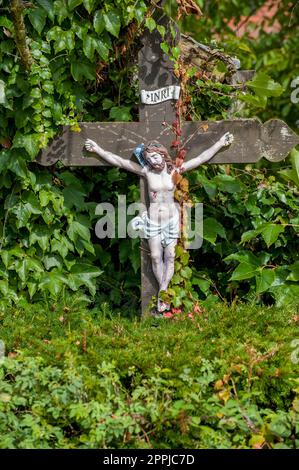 Petite croix en bois avec Jésus au milieu du feuillage vert de divers arbres Banque D'Images