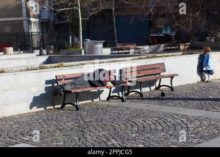 Bucarest, Roumanie - 20 décembre 2022 : sale pauvre sans-abri dort sur un banc du centre-ville. Banque D'Images