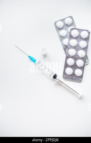 Préparation pour la vaccination contre le covid-19. Seringue, vaccin, pilules, masque médical sur une table blanche. Banque D'Images