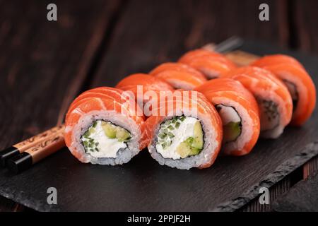 Les sushis roulent philadelphie avec du saumon et du concombre avec de l'avocat et du fromage à la crème sur fond noir. Menu sushi. Concept alimentaire japonais Banque D'Images