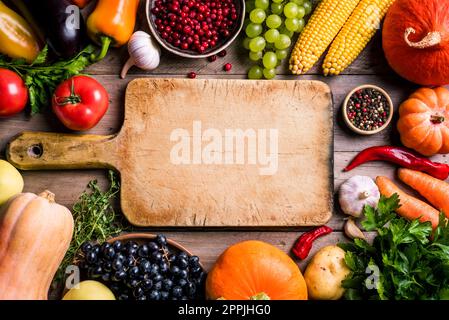 Divers légumes biologiques et planche à découper vide sur table en bois, espace de copie. Cuisiner des aliments biologiques sains de fond. Récolte d'automne légumes agricoles Banque D'Images