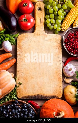 Divers légumes biologiques et planche à découper vide sur table en bois, espace de copie. Cuisiner des aliments biologiques sains de fond. Récolte d'automne légumes agricoles Banque D'Images