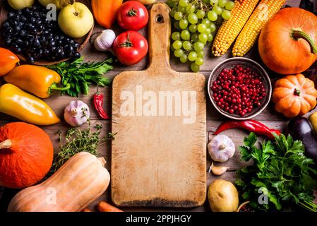 Divers légumes biologiques et planche à découper vide sur table en bois, espace de copie. Cuisiner des aliments biologiques sains de fond. Récolte d'automne légumes agricoles Banque D'Images