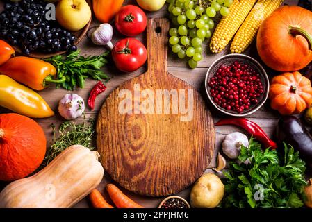 Divers légumes biologiques et planche à découper vide sur table en bois, espace de copie. Cuisiner des aliments biologiques sains de fond. Récolte d'automne légumes agricoles Banque D'Images