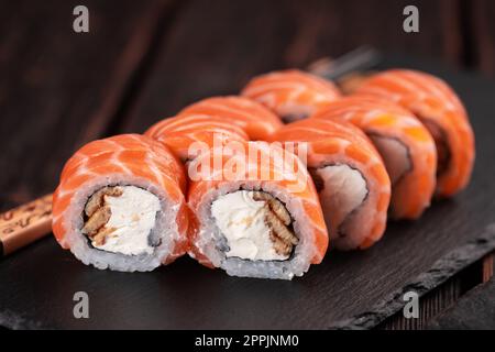Les sushis roulent philadelphie avec du saumon et de l'anguille et du fromage à la crème sur fond noir. Menu sushi. Concept alimentaire japonais Banque D'Images