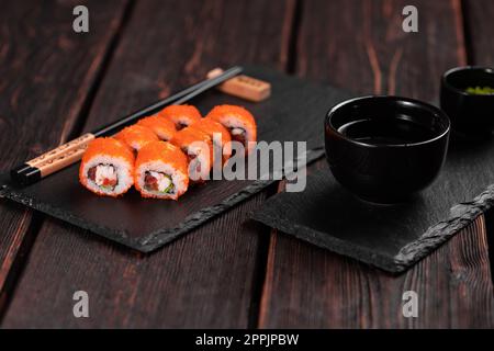 Un petit pain de sushis aux crevettes et au poivron rouge et un tobiko caviar avec salade servi sur un tableau noir en gros plan - de la cuisine japonaise Banque D'Images