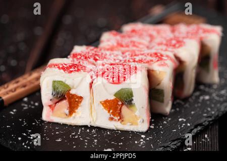Gros plan sur les sushis maki sucrées asiatiques - roulez avec des fruits et du fromage à la crème avec des flocons de noix de coco et de la garniture Banque D'Images