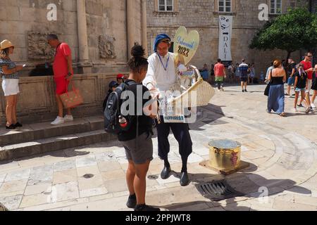 Dans les rues de Dubrovnik Croatie, des vacanciers heureux marchent et achètent des souvenirs du vendeur dans le costume croate festif national le 15 août 2022. Industrie touristique. Journée d'été. Vente de marchandises Banque D'Images