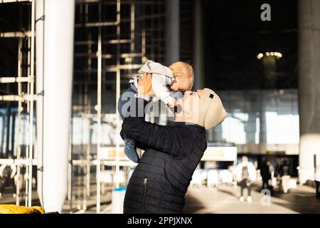 Père heureux tenant et soulevant son bébé garçon enfant en l'air après avoir été rejunted devant la gare de l'aéroport. Concept de voyage pour bébé. Banque D'Images