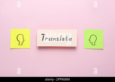 Carte avec mot Translate entre les notes adhésives avec des têtes humaines dessinées sur fond rose, couché à plat Banque D'Images