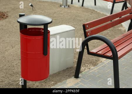 Poubelle en métal rouge près d'un banc en bois dans le parc de la ville Banque D'Images