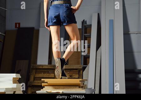 Vue arrière des jambes d'une femme dans les vêtements de travail sur une pile de dalles de panneaux de particules Banque D'Images