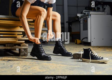 Jambes féminines dans l'atelier de charpentier, changement de chaussures nouant la dentelle Banque D'Images