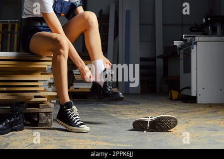 Femme méconnaissable changeant de chaussures dans l'atelier de charpentier Banque D'Images