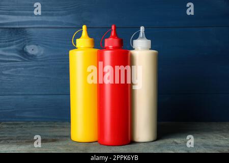 Bouteilles de moutarde, ketchup et mayonnaise sur table en bois bleu Banque D'Images