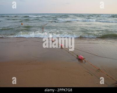 Bouées sur une corde près de l'eau de mer. Les bouées sont des attaches roses pour alerter les gens de la profondeur de l'eau. Sauvetage de la noyade. Délimitant un lieu sur une plage de sable entre les hôtels. Vague avec des bulles Banque D'Images