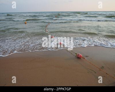 Bouées sur une corde près de l'eau de mer. Les bouées sont des attaches roses pour alerter les gens de la profondeur de l'eau. Sauvetage de la noyade. Délimitant un lieu sur une plage de sable entre les hôtels. Vague avec des bulles Banque D'Images