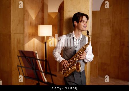 Musicien de jazz jouant du saxophone et se penchant contre le mur du studio d'art Banque D'Images