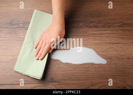 Femme essuyant du lait renversé avec une serviette en papier sur une surface en bois, vue de dessus Banque D'Images