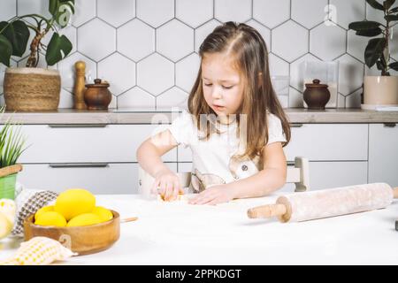 Portrait de petite fille chef sérieux, aidant, faisant la forme de pâte biscuits de pâques. Sculpter la pâte farine boulangerie tasse biscuit. Banque D'Images