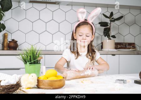 Portrait de petite fille souriante studieusement, cuisine, préparer la pâte, rouleau à pâtisserie avec de la farine. Faire des biscuits de boulangerie de pâques Banque D'Images