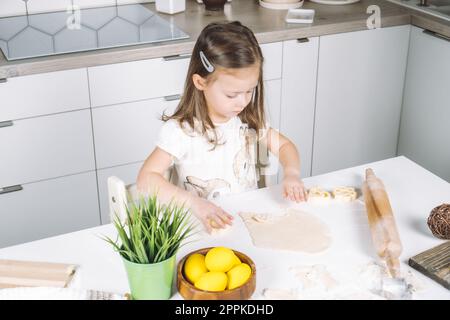 Portrait de chef de petite fille concentrée, sculptant des biscuits en forme de pâte, tasse à pâtisserie. Préparation d'événement de vacances de Pâques Banque D'Images