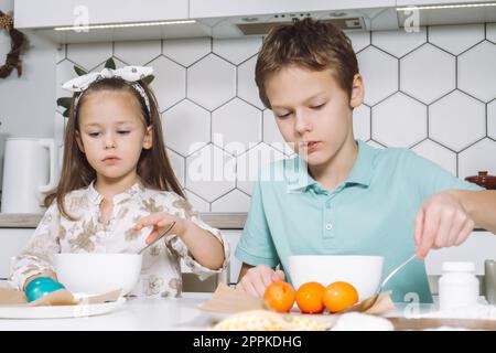 Portrait concentré deux petits enfants, garçon, fille, coloriant les œufs de poule de Pâques. Absorber, couleur d'absorption. Gros plan Banque D'Images