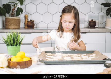 Portrait de petite fille studieusement enfant, chaise assise cuisine, faire différents biscuits de pâte de forme de pâques, poêle à égoutter Banque D'Images