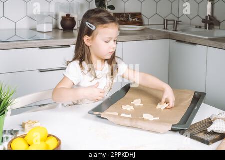 Portrait de petite fille studieusement enfant, chaise assise cuisine, faire différents biscuits de pâte de forme de pâques, poêle à égoutter Banque D'Images