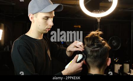 coiffure pour hommes et coupe de cheveux avec tondeuse à cheveux dans un salon de coiffure ou de coiffure. Service de coiffeur dans un salon de coiffure moderne dans un éclairage sombre clé avec vue arrière de lumière chaude Banque D'Images