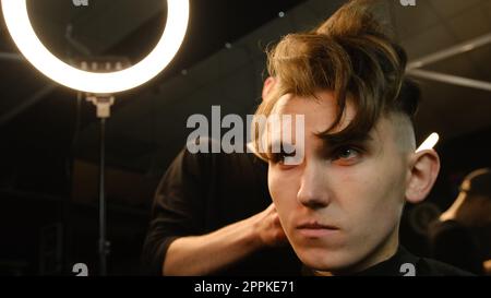 coiffure pour hommes et coupe de cheveux avec tondeuse à cheveux dans un salon de coiffure ou de coiffure. Service de coiffeur dans un salon de coiffure moderne dans un éclairage sombre clé avec vue de face de lumière chaude Banque D'Images