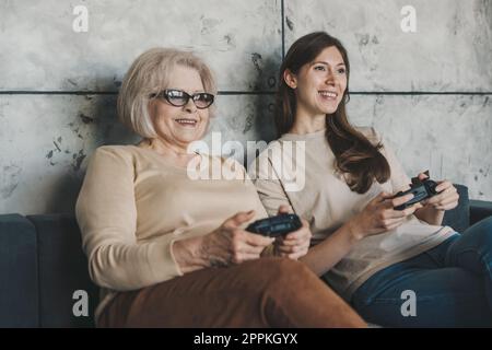 Jeux vidéo concurrence en famille entre deux femmes de différentes générations. Passer un moment de loisir à la maison avec une mère qui s'occupe de lui. Banque D'Images
