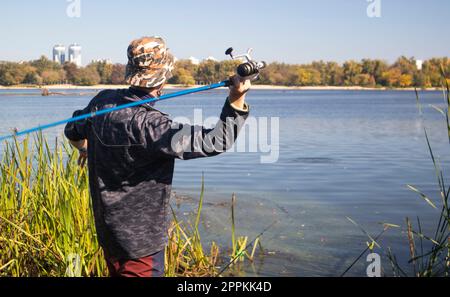 Un pêcheur mâle a jeté une canne à filer dans un lac ou une rivière par une journée ensoleillée. Pêche côtière. Un pêcheur sur la rive de la rivière tient une tige dans sa main. Le concept de repos de pays. Article de pêche. Banque D'Images