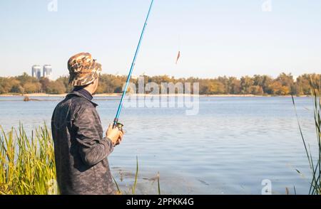 Un pêcheur mâle a jeté une canne à filer dans un lac ou une rivière par une journée ensoleillée. Pêche côtière. Un pêcheur sur la rive de la rivière tient une tige dans sa main. Le concept de repos de pays. Article de pêche. Banque D'Images