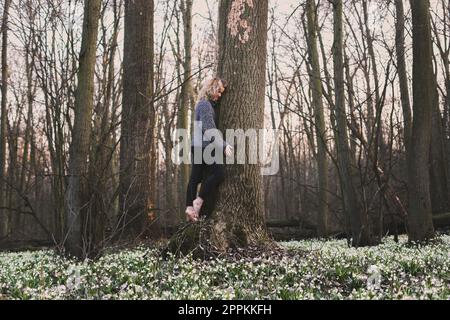 Femme blonde embrassant grand tronc d'arbre photographie pittoresque Banque D'Images