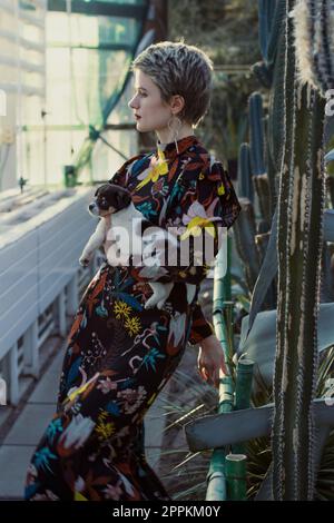 Dame en robe longue tenant le chiot dans le jardin botanique photographie pittoresque Banque D'Images