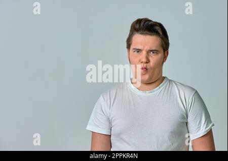 un homme puffant ses joues avec un visage drôle sur un fond gris, des émotions Banque D'Images