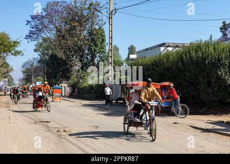 Vélo de rickshaw traditionnel avec des Malgaches dans la rue d'Antsirabe, l'un des moyens de gagner de l'argent. La vie quotidienne dans les rues de Madagascar. Banque D'Images